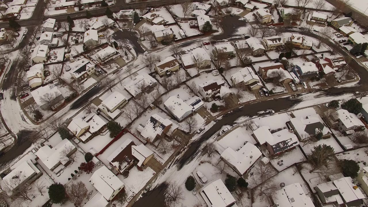 Aerial view of a snow-dusted neighborhood with houses and winding roads.