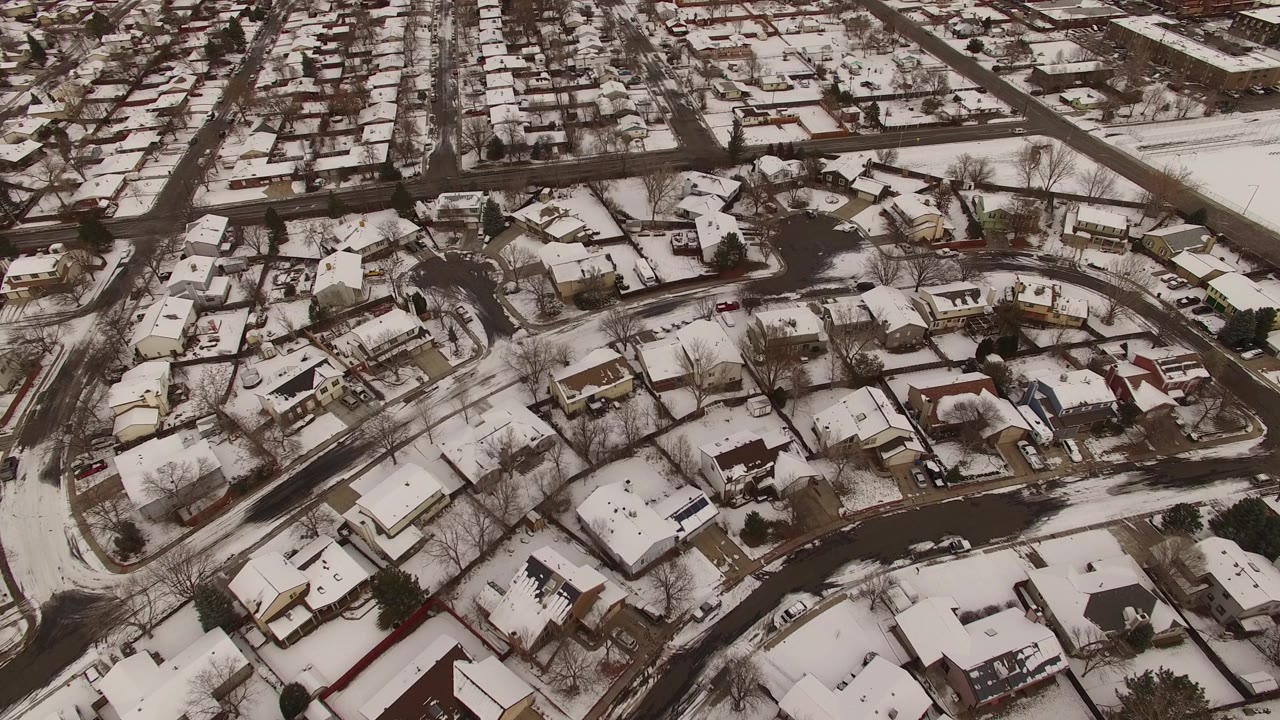 High oblique aerial frame over Jefferson County, Colorado houses with white roofs, dark roadways, bare winter trees, and no visible people.