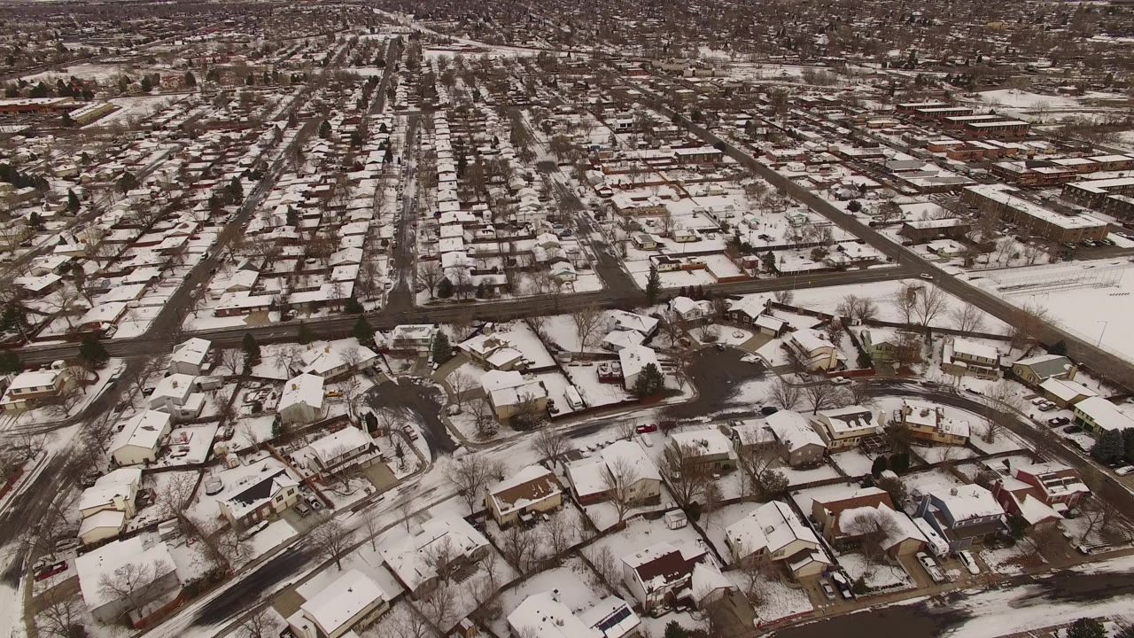 High aerial frame of Jefferson County, Colorado homes with white roofs, curving side streets, a straight road running toward the horizon, and no visible people.