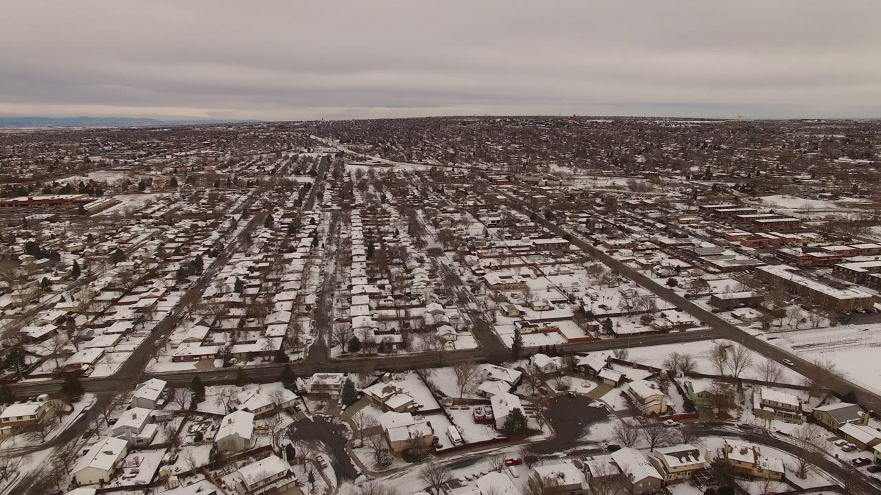 Wide aerial view over Jefferson County, Colorado homes with snow-dusted roofs, gridded streets, and no visible people at the opening frame.