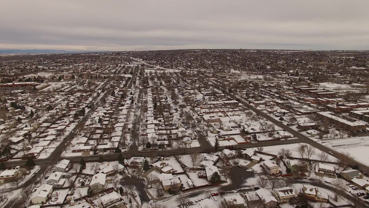 Elevated view across Jefferson County, Colorado showing rows of houses, pale snow patches, dark road lines, and no visible people near the early part of the clip.