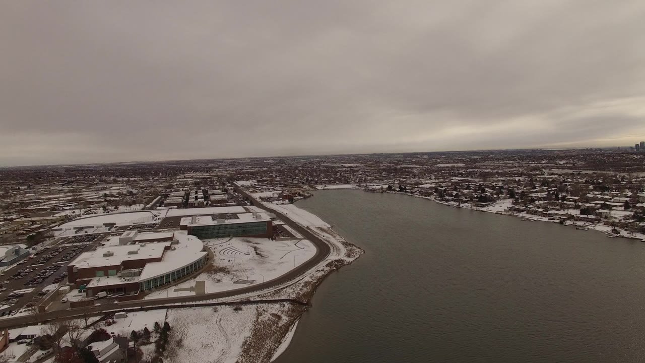 Snowy waterfront district beside dark water under gray clouds.