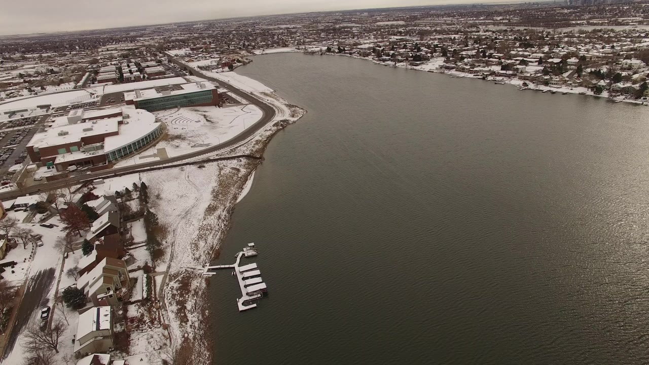 Snowy shoreline homes, docks, and wide water from above.