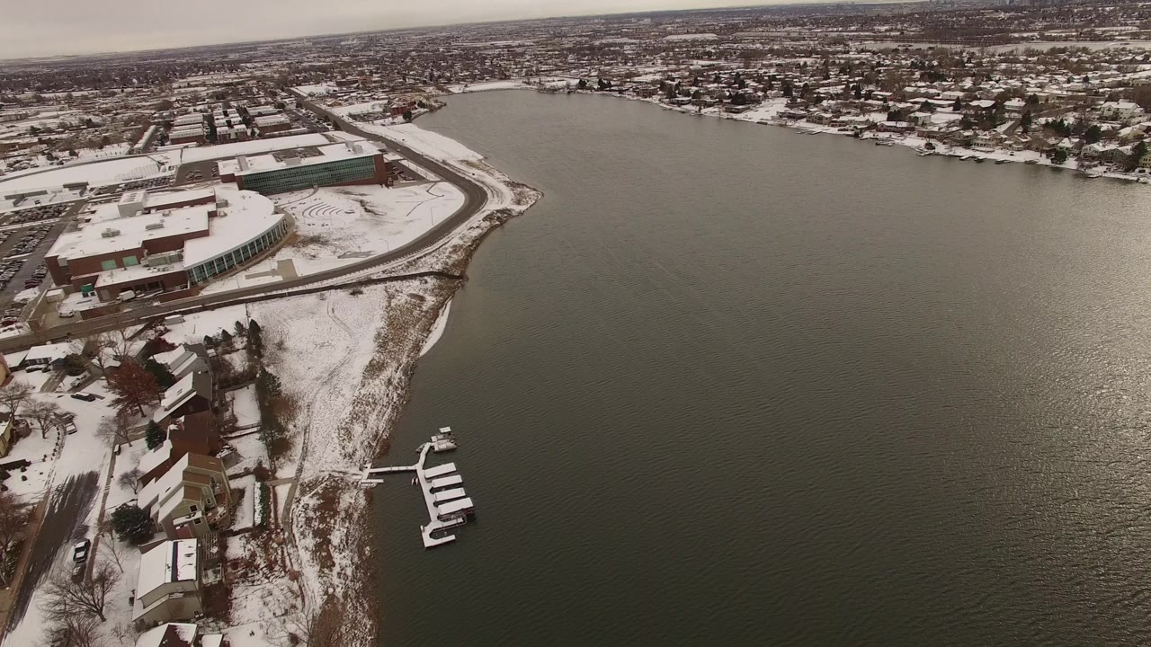 Aerial frame in Jefferson, Colorado showing the shoreline running down the image, clustered homes and docks at the water's edge, muted winter light, and no visible people.