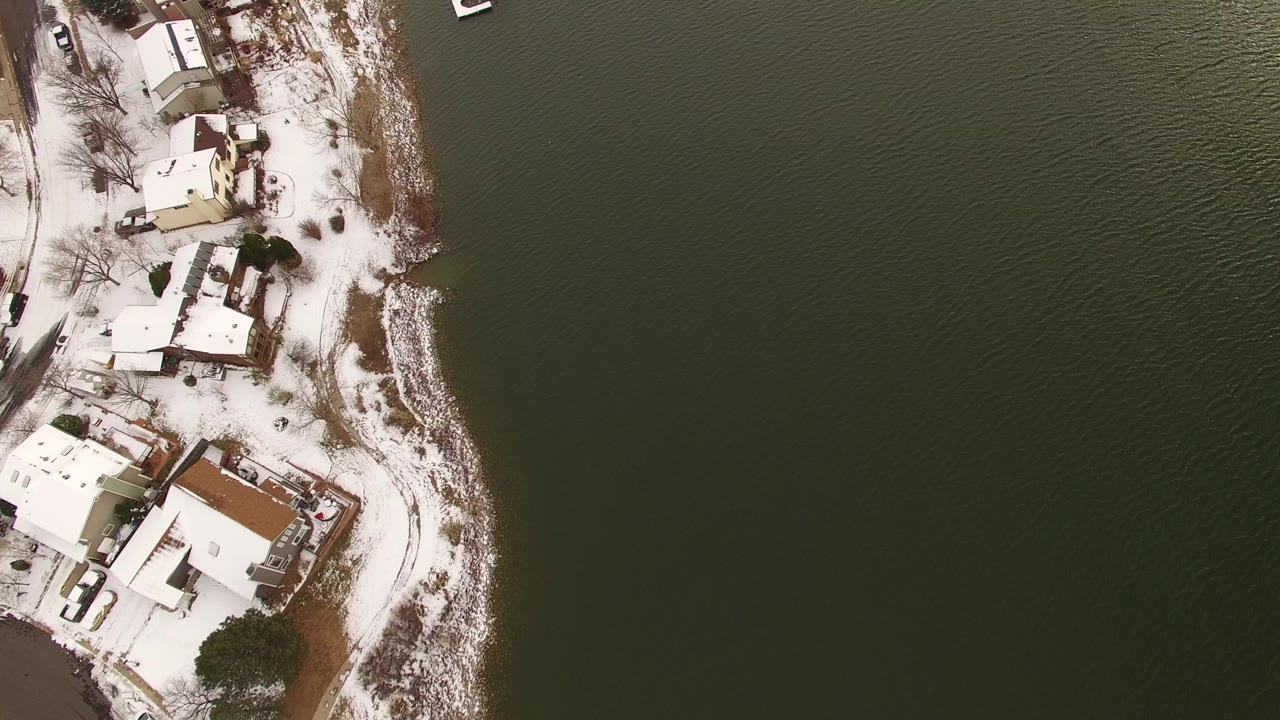 Overhead snowy lakeside homes beside dark water.