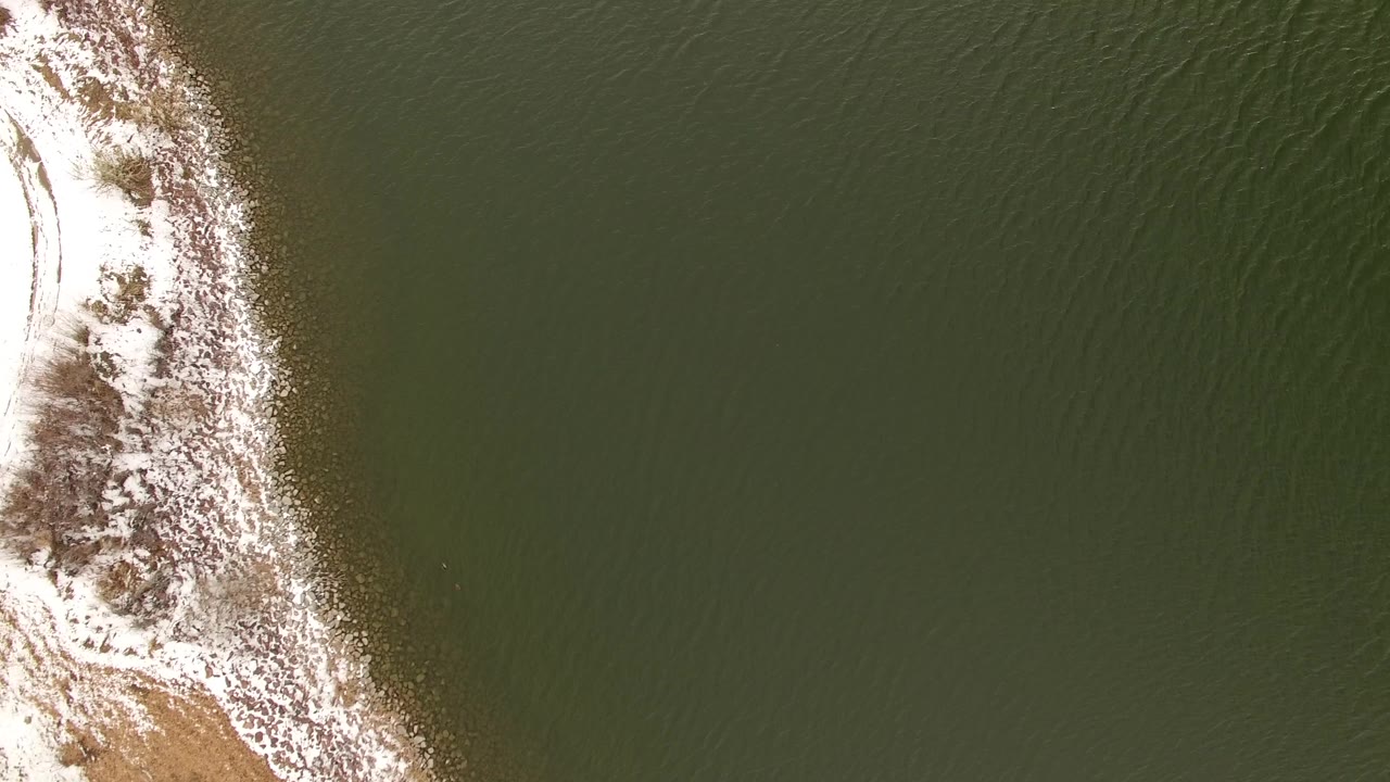 Narrow snowy shoreline separates green water from land.
