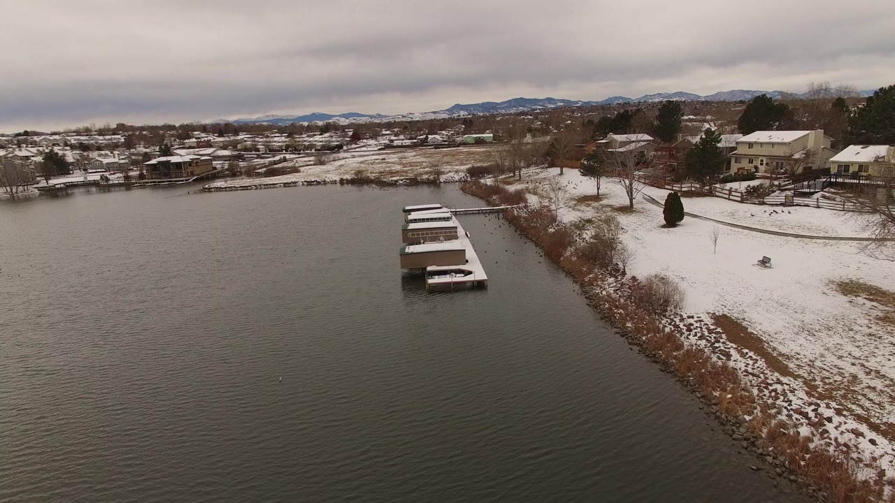 Snowy lake shoreline with docks, houses, and distant mountains