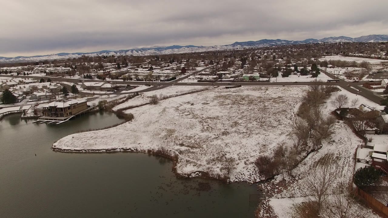 Snowy suburban lakefront with houses, roads, and distant foothills