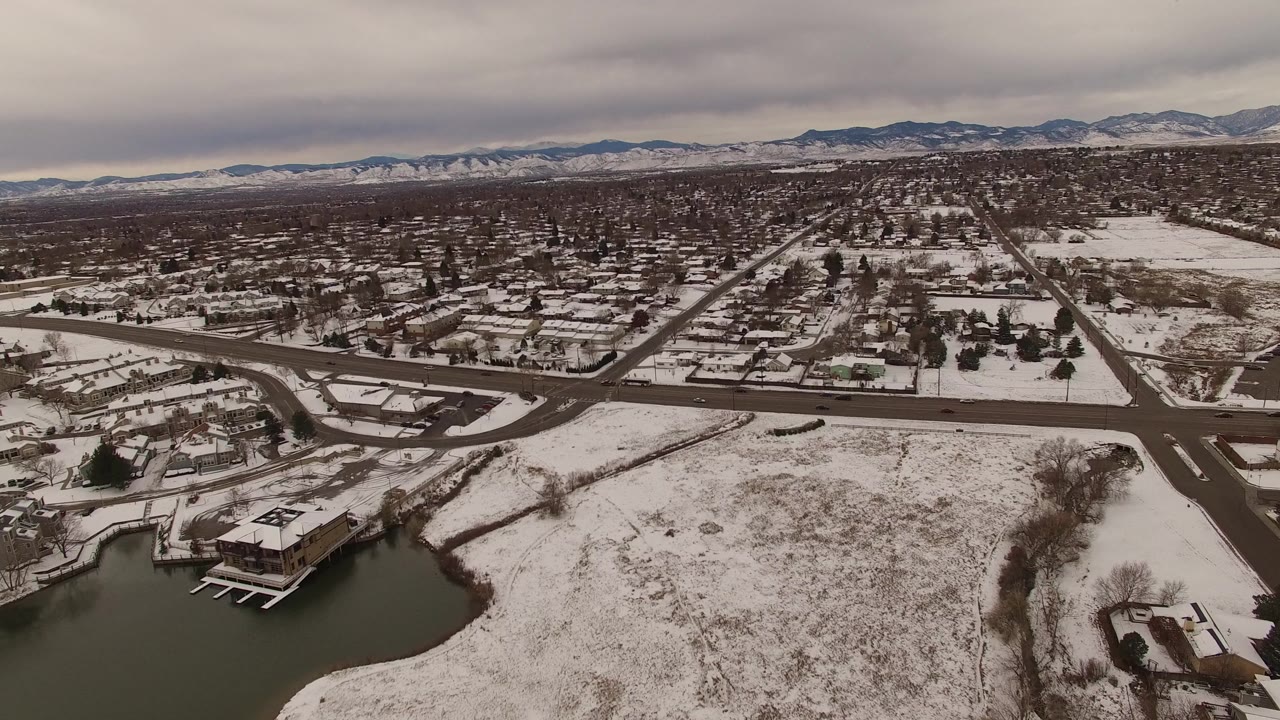 Snowy residential aerial view with roads, lake edge, and mountains