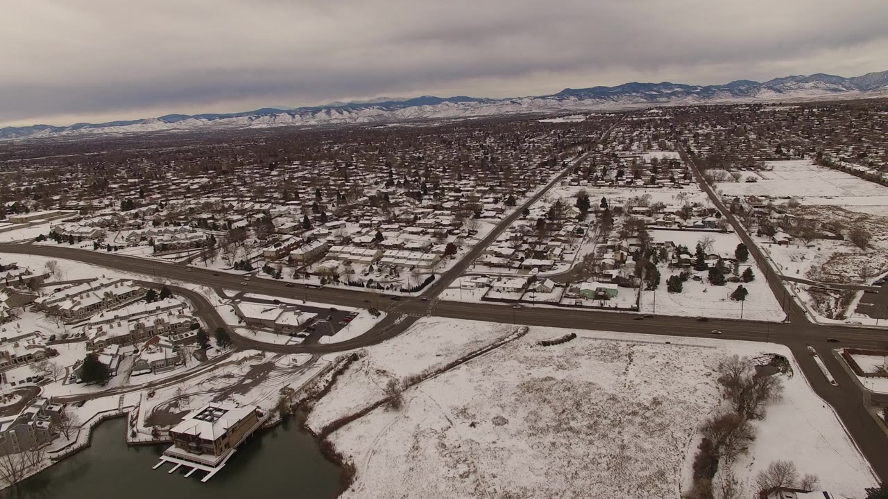 At 0:01, the Jefferson County aerial view keeps the dark road grid prominent against snow-covered homes and open parcels, with distant mountains and no visible people.