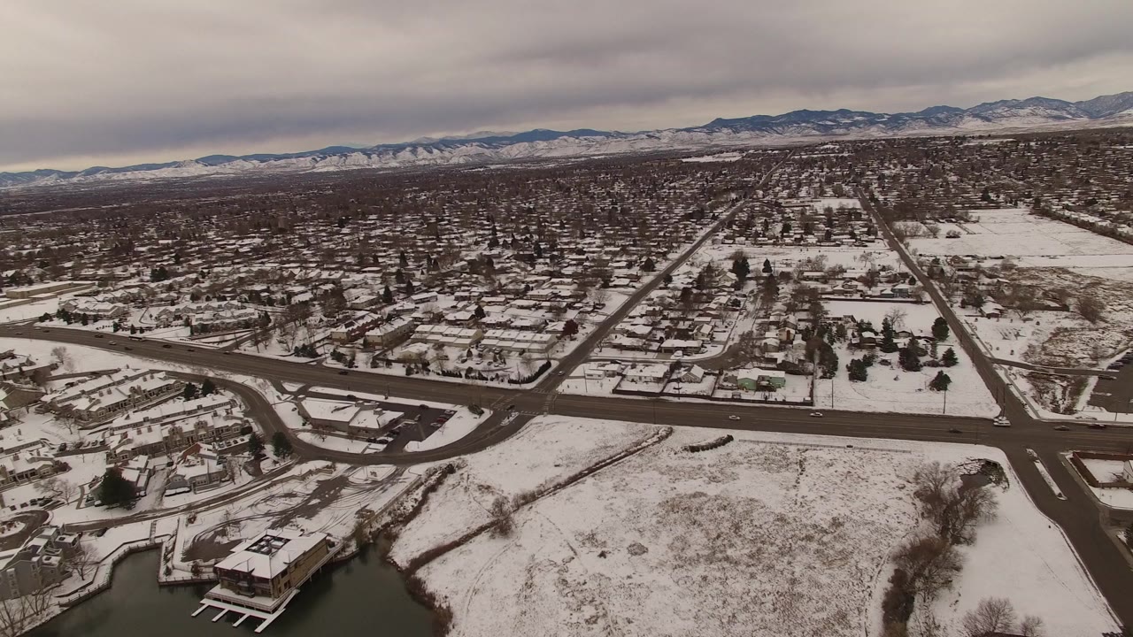 Elevated view in Jefferson County, Colorado, showing empty dark roads cutting through snowy residential blocks, open white fields, distant ridges, and no visible people.