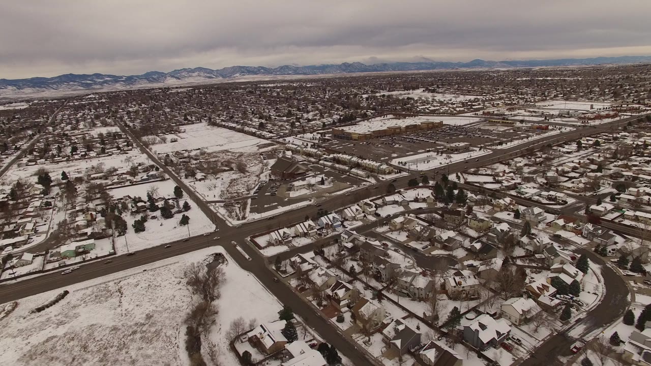 Elevated Jefferson County, Colorado view with snow on roofs and lots, a broad road junction in the foreground, open fields to the left, and no visible people.