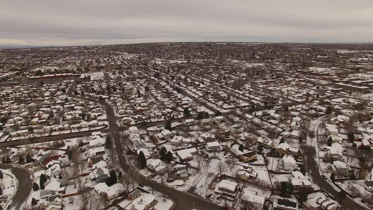 Jefferson County, Colorado neighborhood grid viewed from above, with white rooftops, dark wet roads, leafless trees, parked cars, and no visible people.