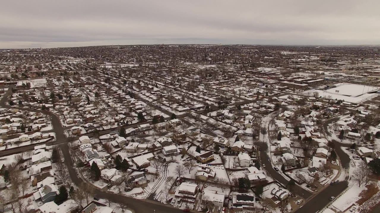 Wide snowy suburb with streets and low buildings under gray sky.