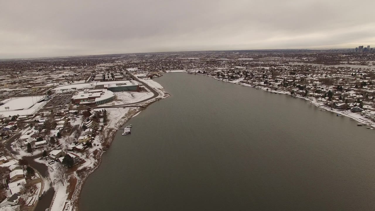 Snowy residential shoreline beside a broad gray body of water