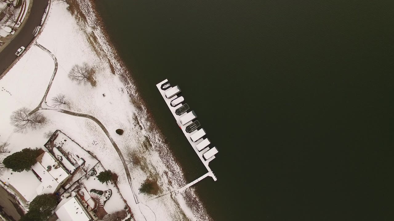 Overhead view in Jefferson, Colorado of dark water, a snow-covered shoreline, a small dock, curved paths, bare trees, and nearby houses, with no visible people.