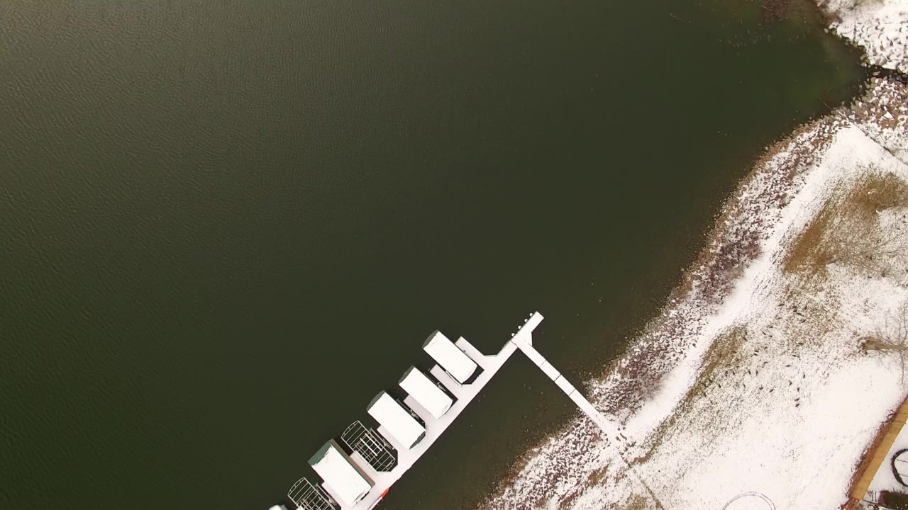 Overhead Jefferson, Colorado frame with dark green lake water on the left, a snow-covered shore on the right, a diagonal dock cluster near the lower left, and no visible people.