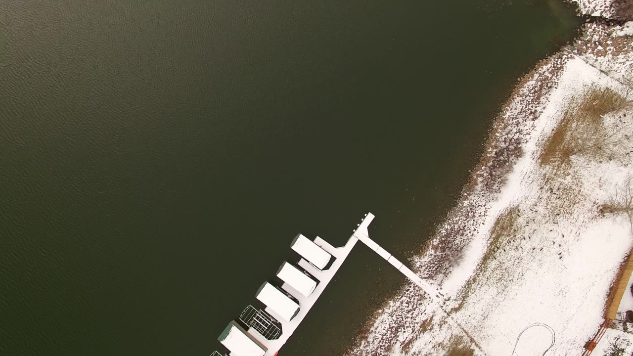 Top-down lake edge with white docks, snow, and a curved shoreline path area.