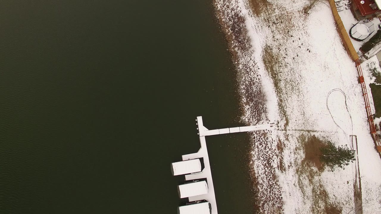 Overhead view of snowy shoreline, dark water, and white docks.