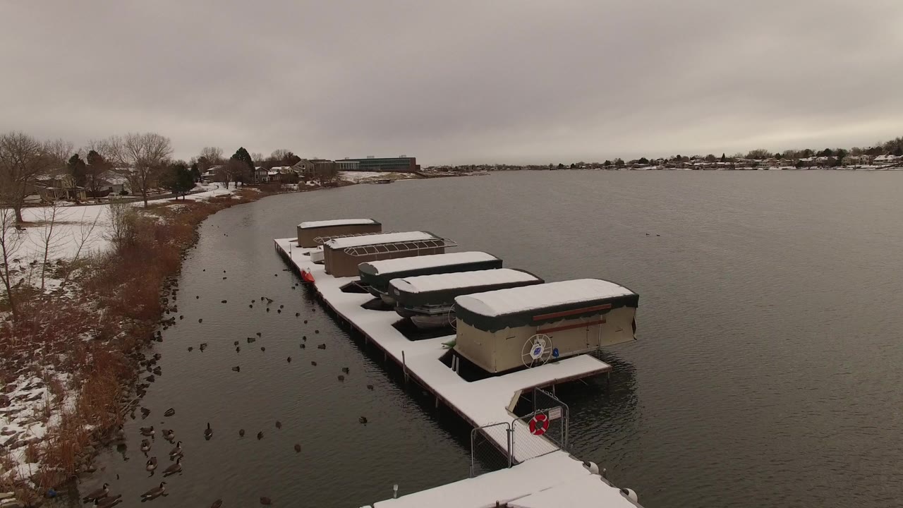 Snow-covered boats docked along a lake shoreline under gray winter sky.