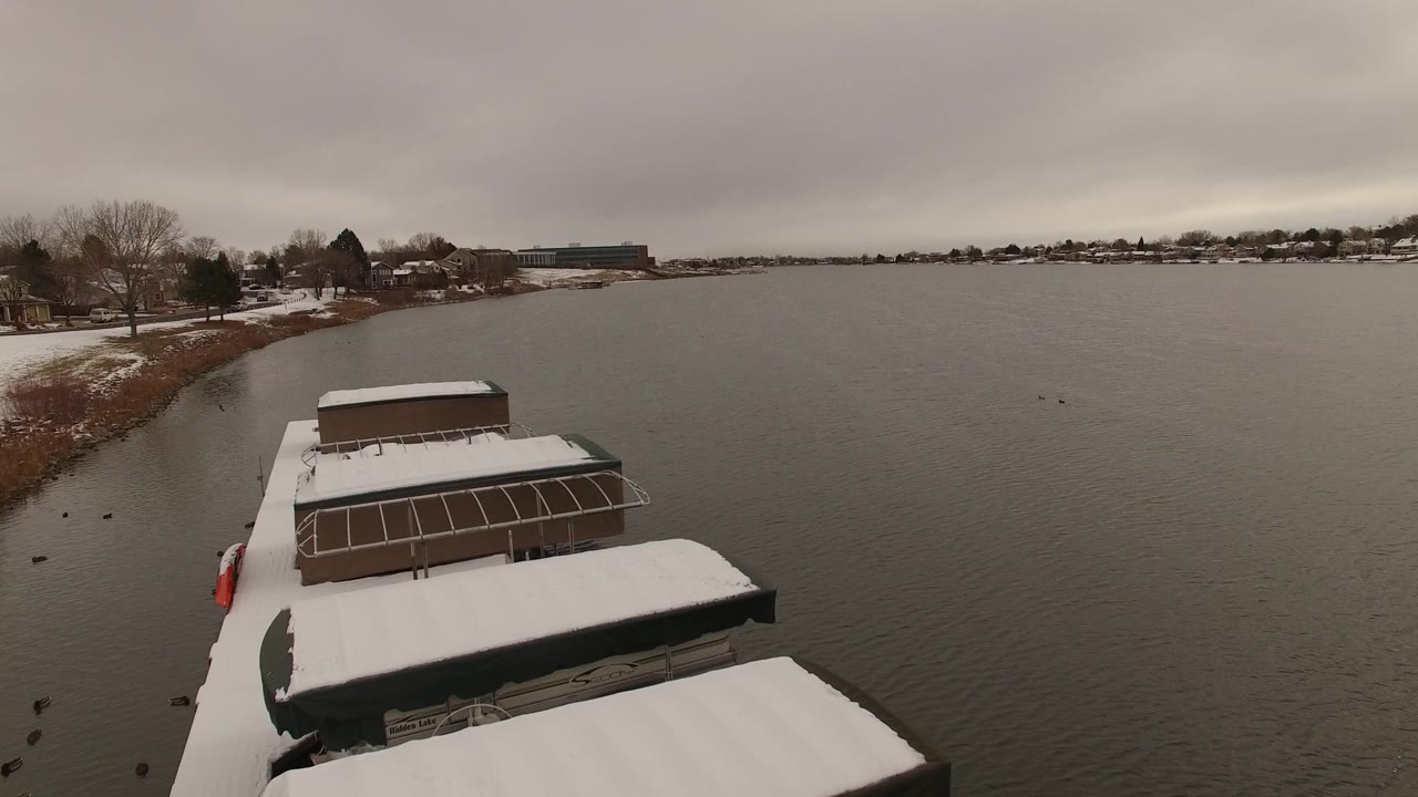 Elevated Jefferson County, Colorado lake view with docked boats closer to center, rippled gray water to the right, snowy shoreline to the left, and no visible people.