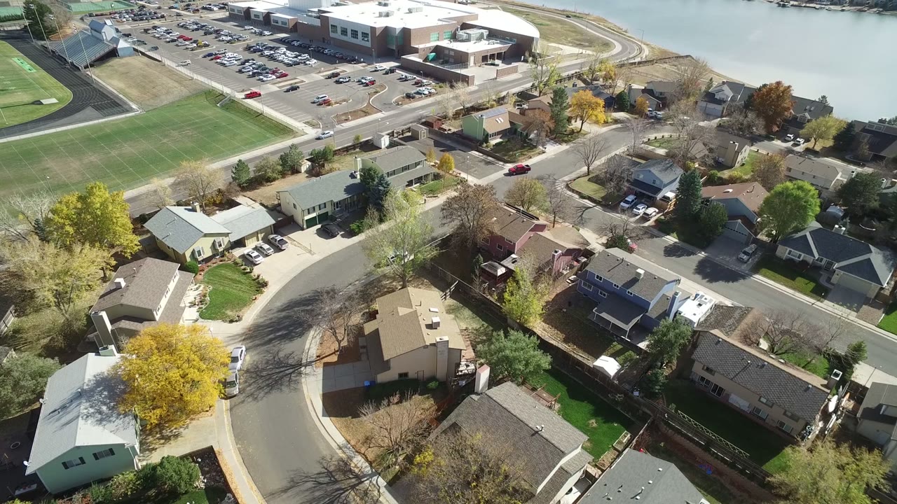 Aerial view of homes, curved streets, a sports field, parking lot, and water.