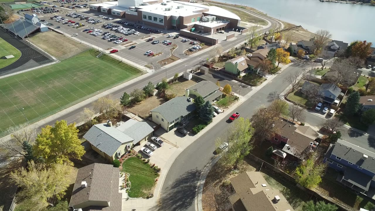 Second aerial frame in Hidden Lake, Colorado, showing more of the green field at center, the large complex and parking lot beyond it, residential streets below, and no visible people.