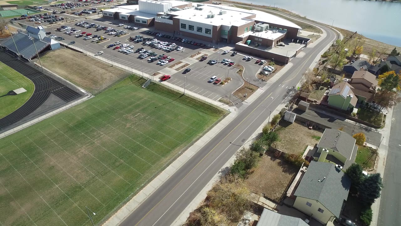 Aerial view of school campus, athletic field, track, roads, parking lot, and houses.