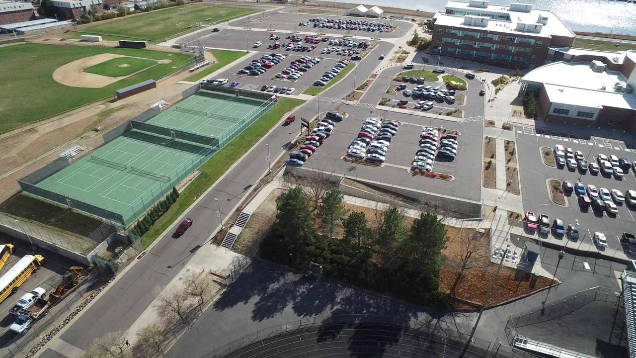 Aerial view of tennis courts, parking lots, campus buildings, roads, and buses.