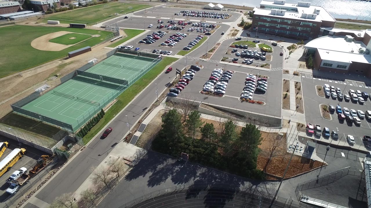 A second aerial frame in Hidden Lake, Colorado holds on the tennis courts and central parking lots, with a baseball field edge, roads, trees, buses, and no visible people.