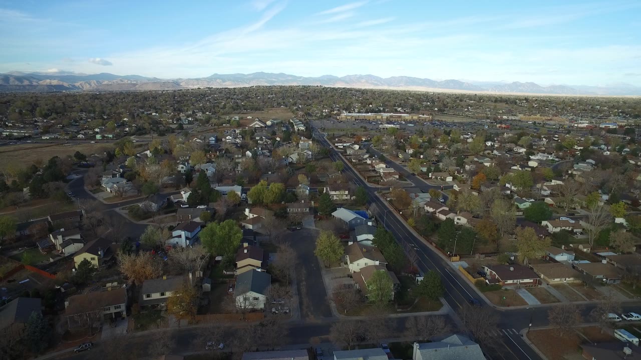 Aerial view in Hidden Lake, Colorado with a main residential road cutting through homes, bare and green trees, open ground, and mountains along the far horizon.