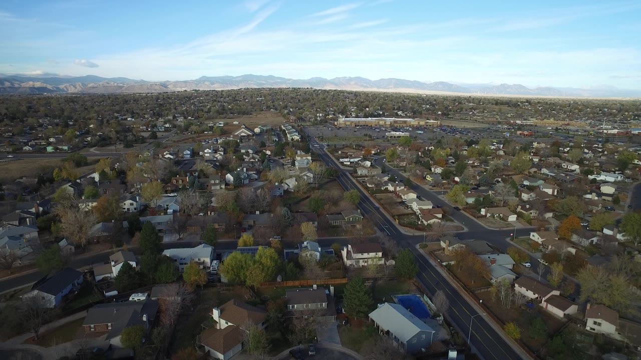 Aerial view over houses, streets, trees, and distant mountains.