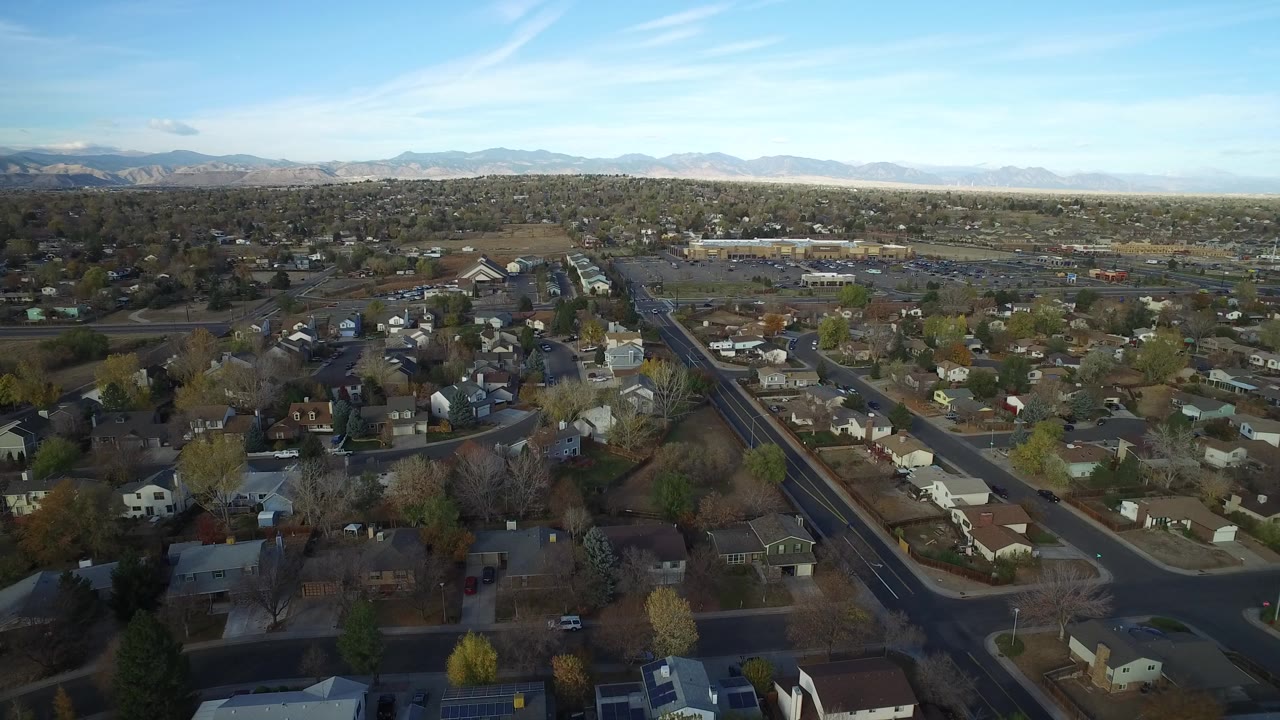 Aerial view over houses, roads, trees, and distant mountains.