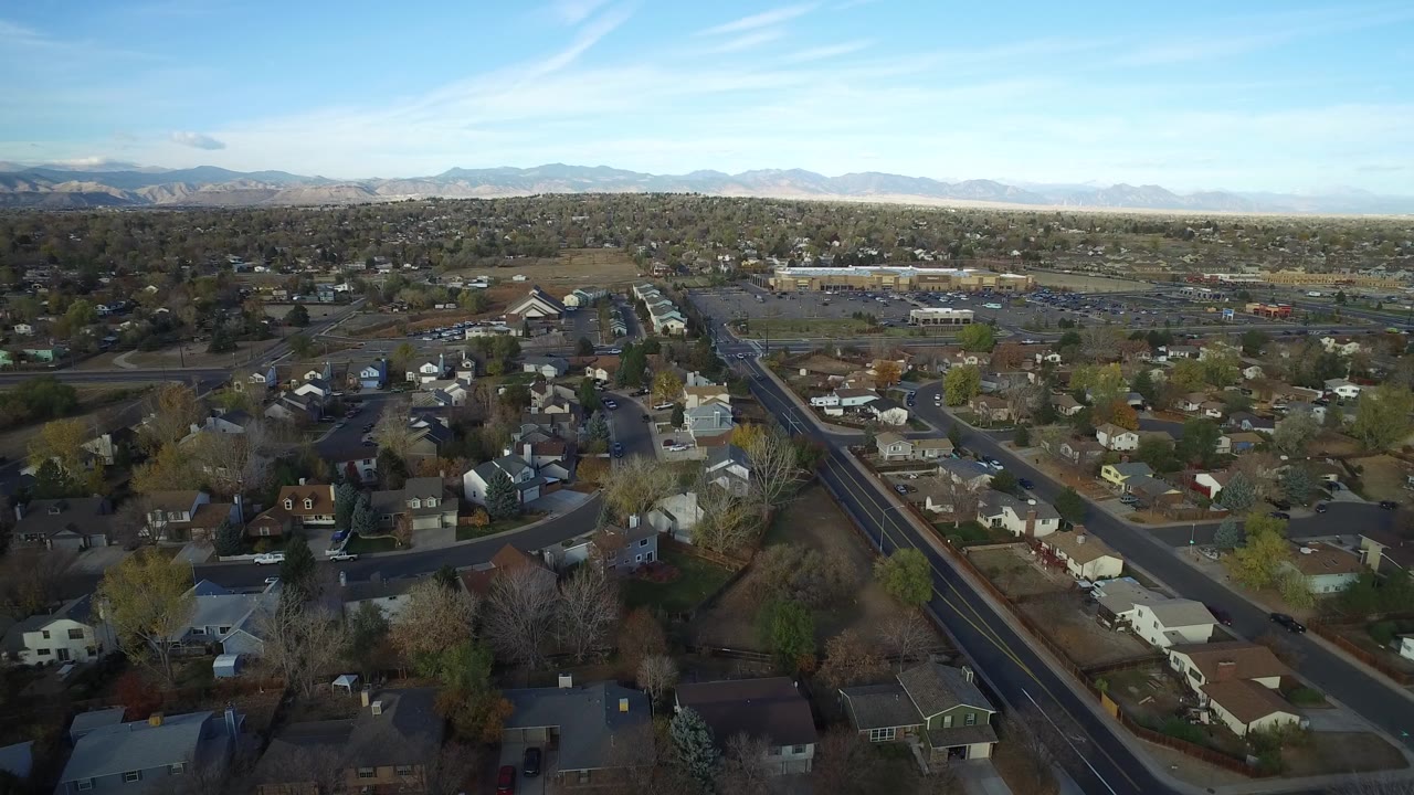A second aerial frame over Hidden Lake, Colorado, keeps the neighborhood grid centered, with a diagonal road, scattered houses, leafless trees, and mountains across the background.