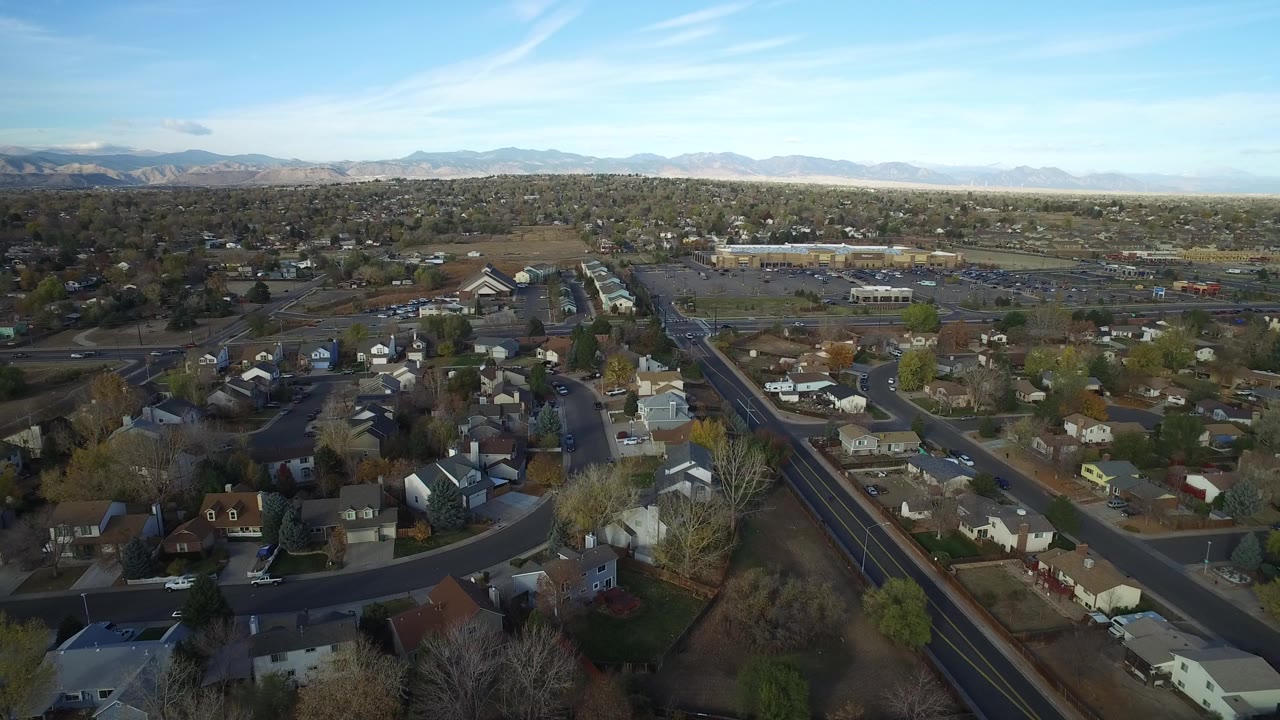 Aerial view over suburban houses, streets, and distant mountains.
