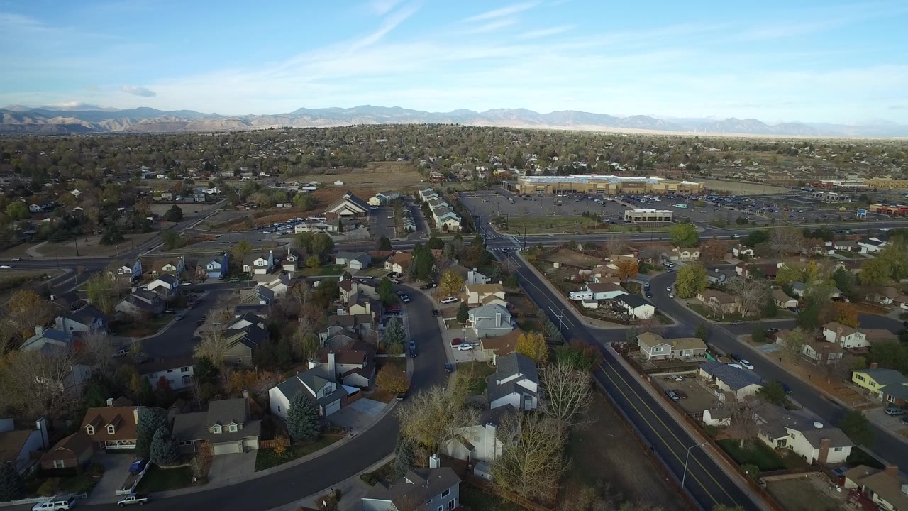 Aerial view over suburban homes, curved streets, trees, and distant mountains.
