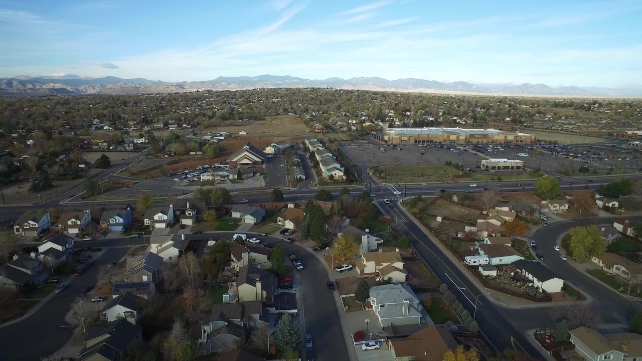 Drone-height view of suburban streets, rooftops, and a mountain horizon.