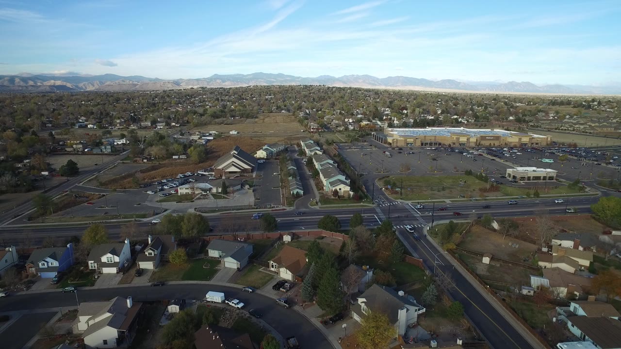 Aerial view of suburban streets, homes, parking lots, and distant mountains.