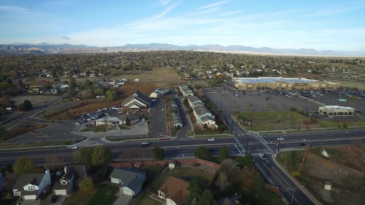Wide drone-style view over traffic lanes, homes, parking lots, and mountains.