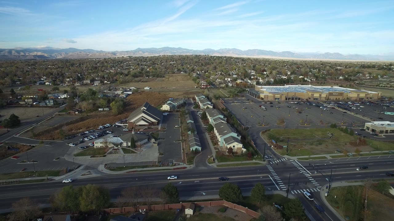 Elevated highway view with moving cars, parking areas, buildings, homes, trees, and mountains.
