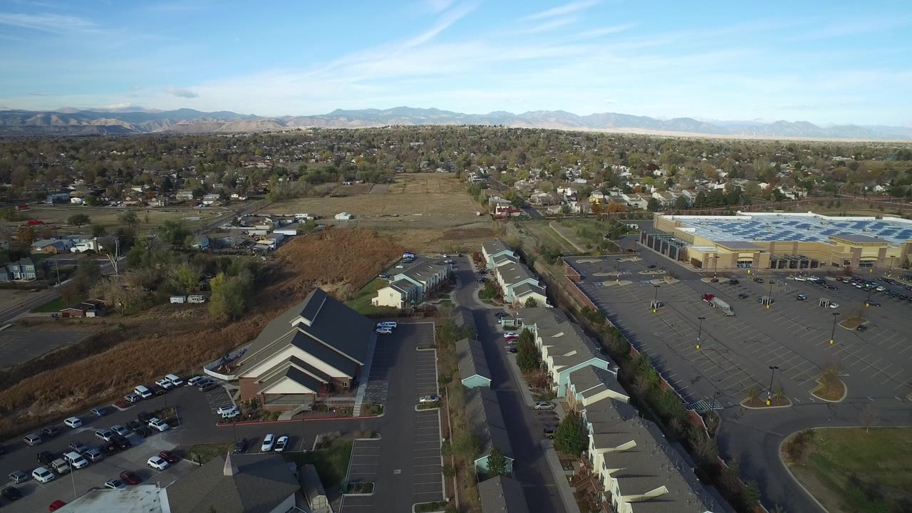Aerial view of parking lots, commercial buildings, homes, open land, and distant mountains.