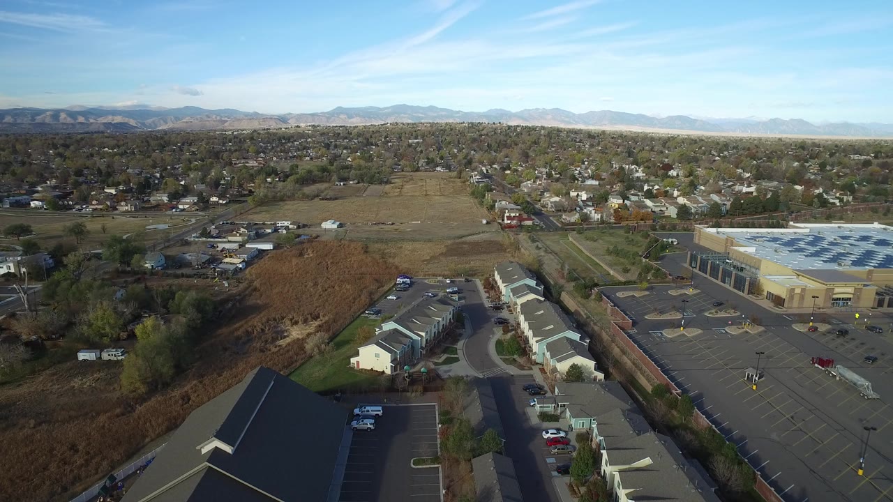 Aerial view of houses, roads, a parking lot, fields, and distant mountains