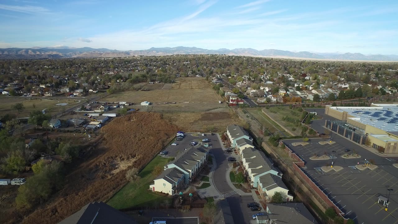 Aerial view over townhomes, a road, parking lots, fields, and distant mountains.