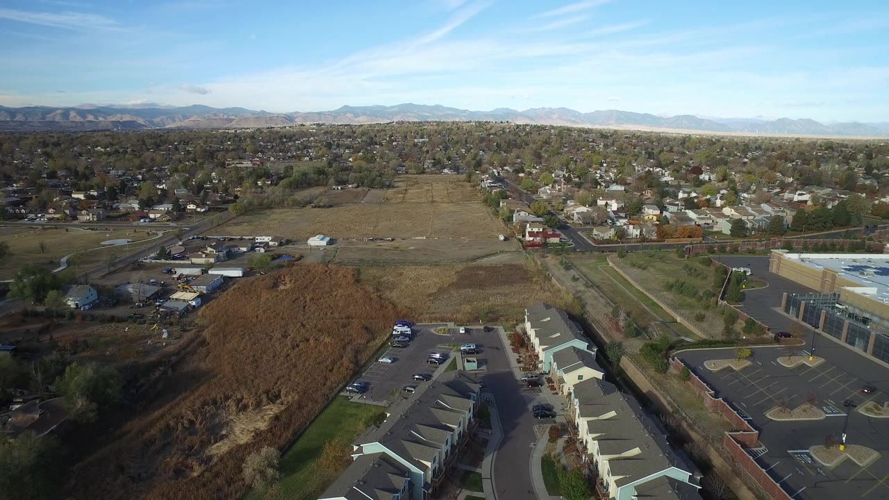 Aerial view over townhouses, parking lots, open fields, homes, and distant mountains.