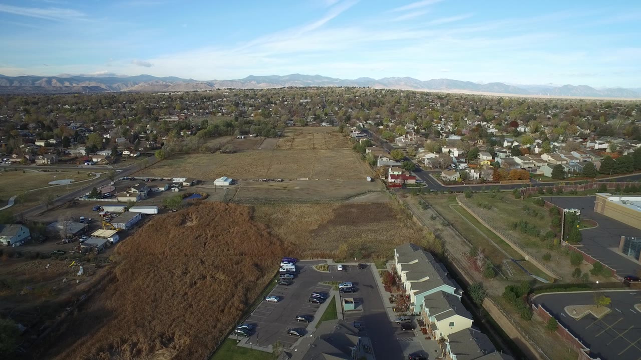 High aerial view in Hidden Lake, Colorado with a broad open lot, neighborhood streets, small buildings, distant mountains, and no visible people.