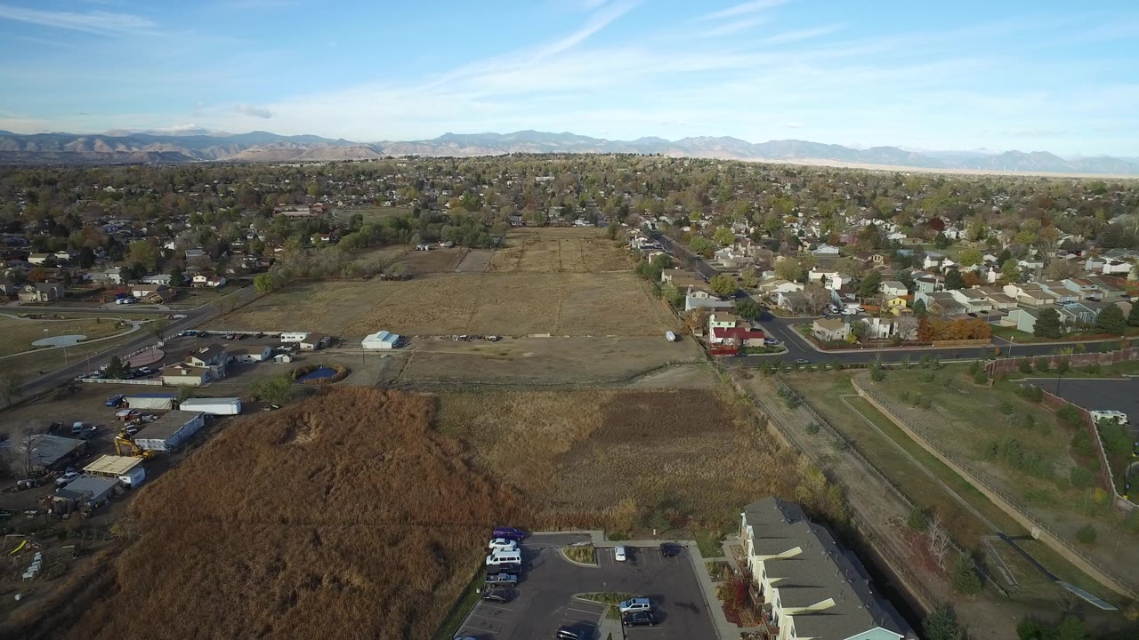 Aerial view of fields, homes, roads, trees, and distant mountains under blue sky.
