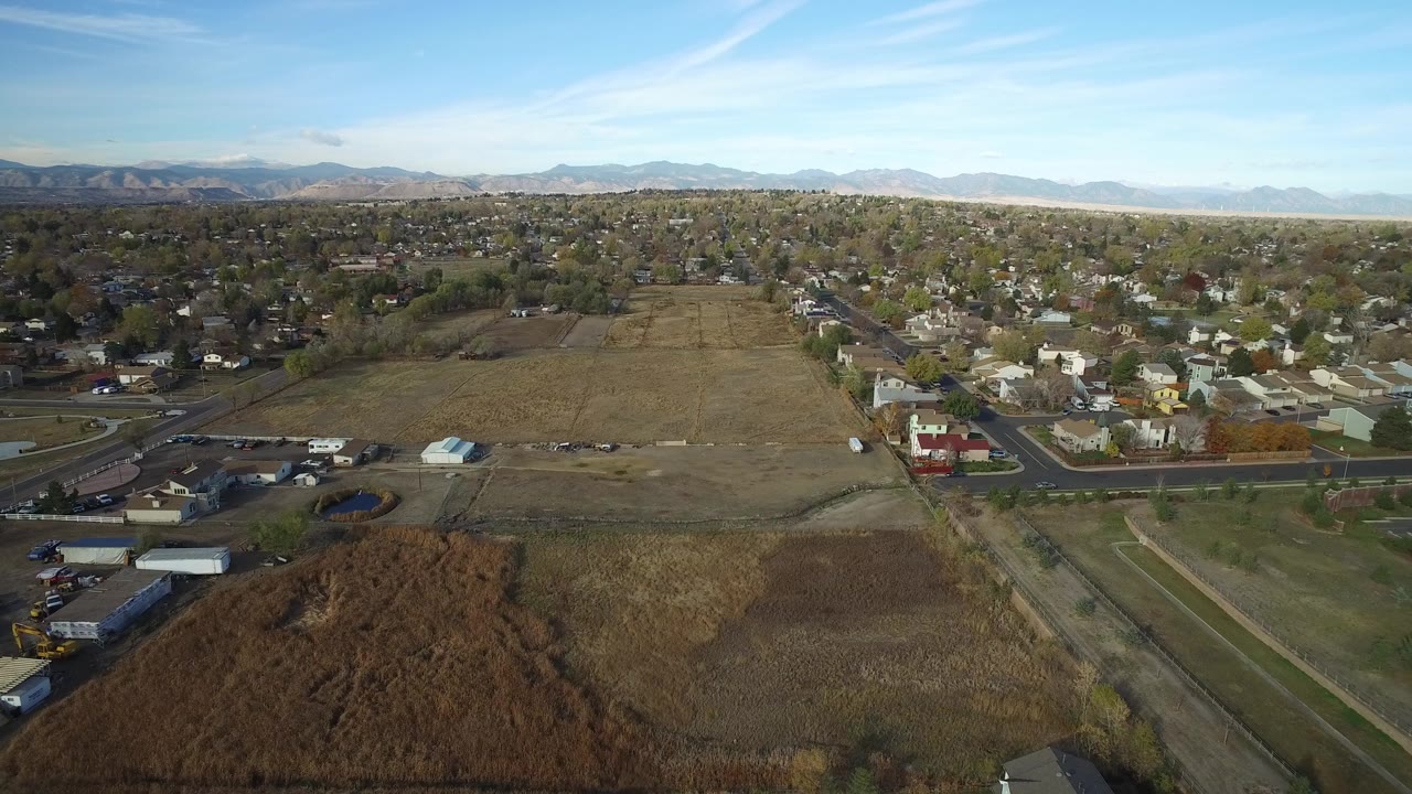 Aerial view over dry fields, roads, homes, and distant mountains.