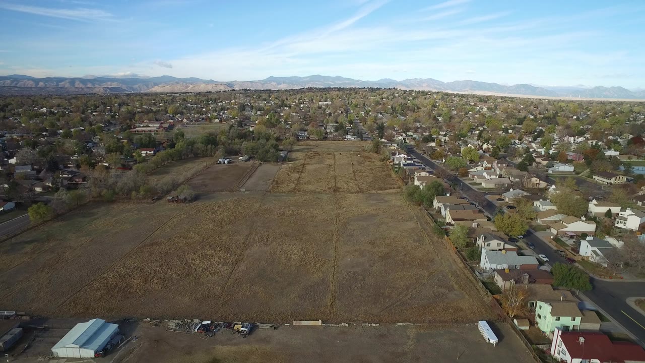 Aerial view of open field beside suburban homes and distant mountains.