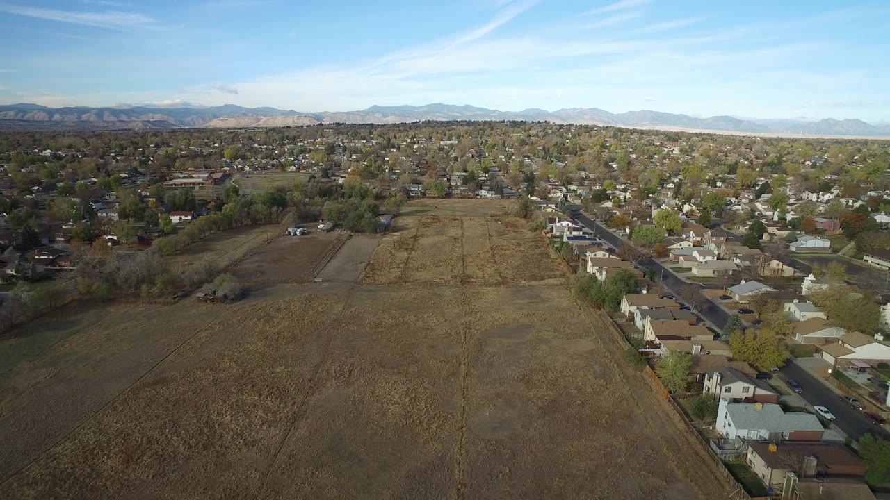 Aerial view of open fields beside a residential neighborhood and distant mountains.
