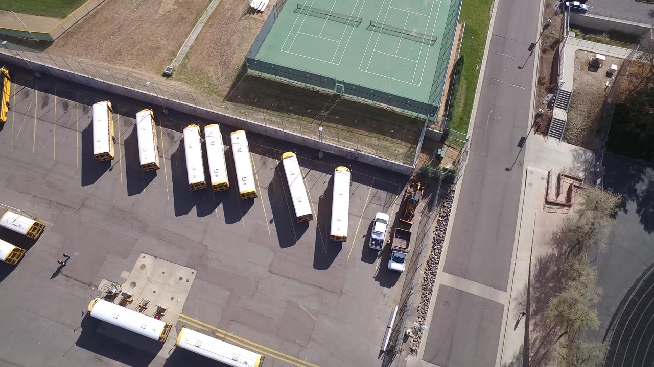 Overhead view of yellow and white lorries parked beside tennis courts.